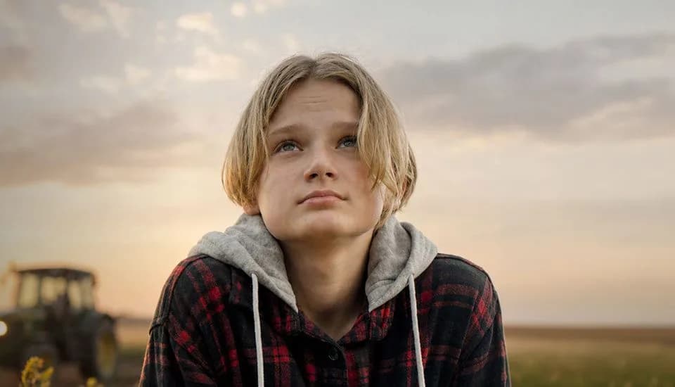 Student in a hoodie looking up in a farm field at sunset, with a tractor behind
