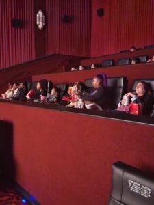 Children and adults watch a movie in a dark theater.