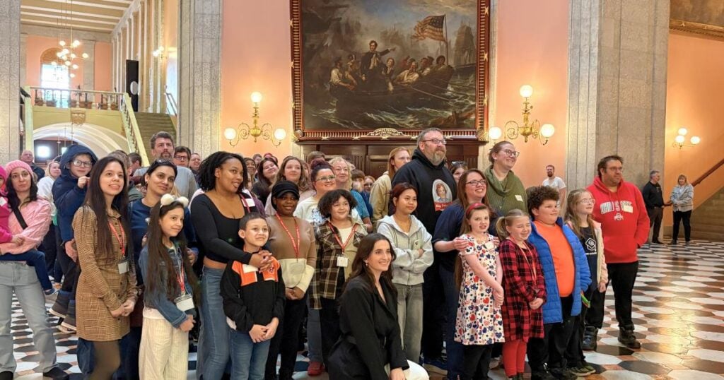 Group of adults and children posing in a large hall with a painting.