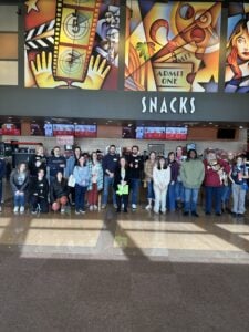 Group of adults and children posing in front of a movie theater snack bar.