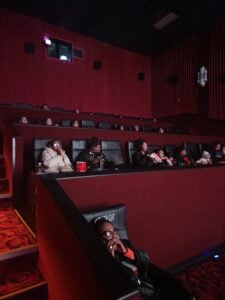 Adults and children watch a movie in a dark theater.